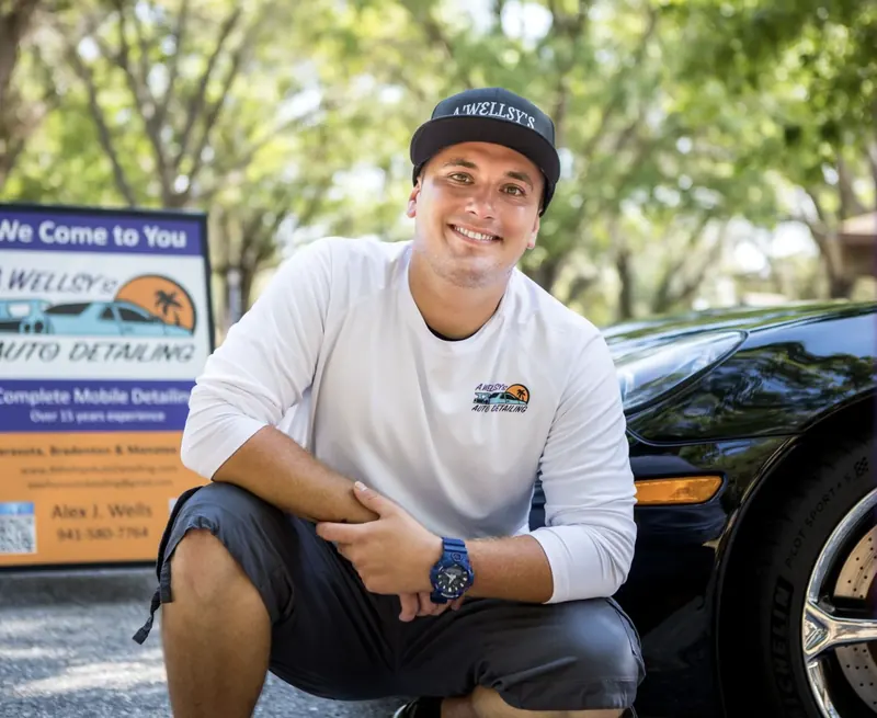 Alex Wells, owner of A'Wellsy's Mobile Auto Detailing, kneeling beside a freshly detailed black sports car